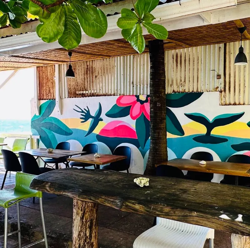 Le patio du restaurant, sa grande table en bois et sa fresque, sous les feuilles de l'arbre