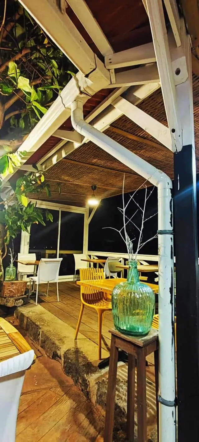 La varangue en bois blanc du restaurant, ses tables et ses plantes, le soir